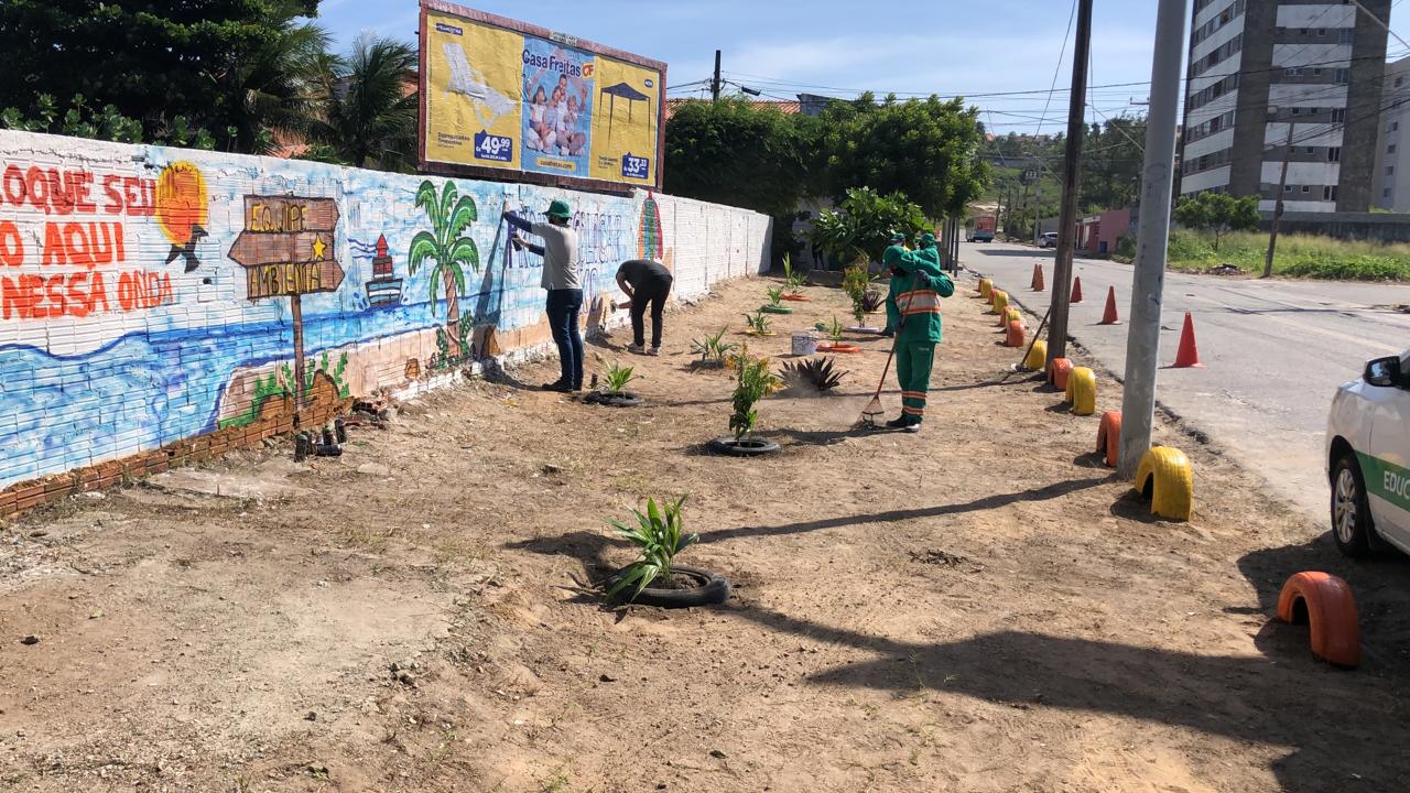 homens limpam um terreno e pintam um muro artístico no local